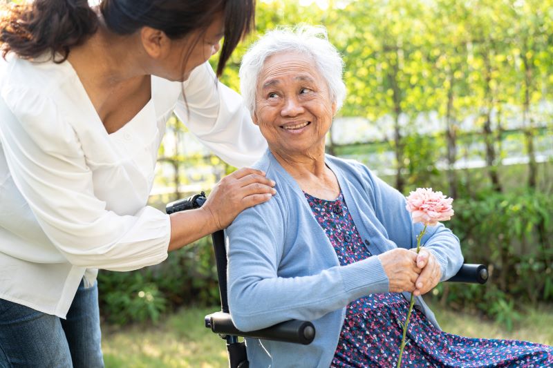 Asian senior woman holding pink rose flower, smile and happy in the sunny garden.